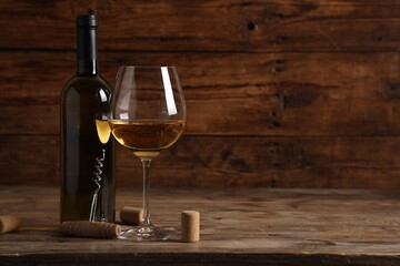 Tasty white wine in glass, bottle, corks and corkscrew on wooden table, space for text