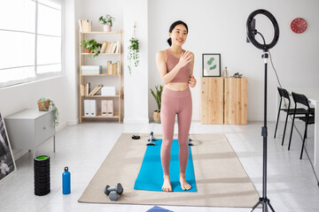 Smiling young social media asian influencer recording video with mobile phone for fitness blog
