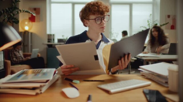 Young man handling paperwork, taking notes, typing on computer and answering phone calls during busy workday in modern office. Time lapse video