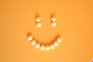 Blister pack of pills and pills arranged in the shape of a smiley face on a yellow background