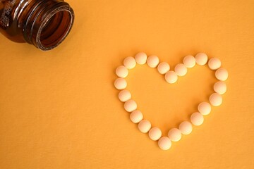 Blister pack of pills and pills arranged in a heart shape on a yellow background