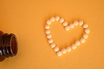 Blister pack of pills and pills arranged in a heart shape on a yellow background