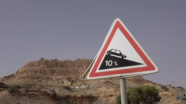 Traffic sign warns drivers for steep road towards the hilltop village of Chenini (visible in the background), transport and history in Tunisia
