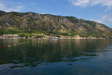 Fototapeta premium A picturesque coastal town nestled against a dramatic mountain range, with a large yacht in the calm waters