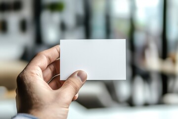 A hand holds a blank business card against a blurred office background, symbolizing networking and professional connections.