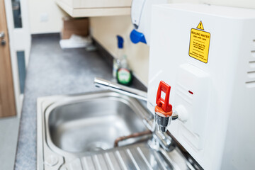 Shallow focus of a hospital instant-boil hot water tap in red. Located on a kitchen sink within an NHS hospital in the UK. Seen in a hospital ward.