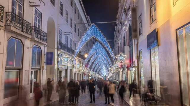 Night timelapse hyperlapse of Christmas lights and decorations in downtown Lisbon at Chiado Carmo street. People walk under illuminated arches. Holiday atmosphere with festive decor in Portugal