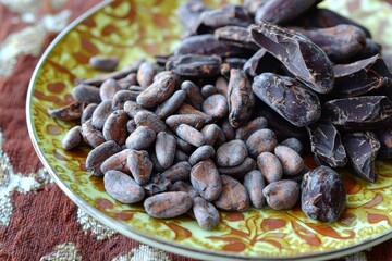 Obraz premium A vibrant plate of raw cocoa beans, some cracked and ready for processing, on a patterned tablecloth, chocolate making ingredient, rustic appeal.
