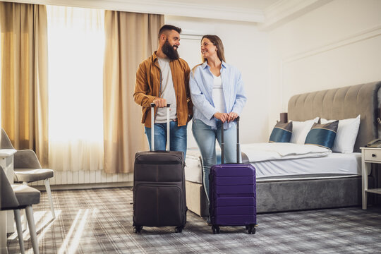 Bearded man and woman with brown hair arrived in hotel. Couple standing in hotel room with their suitcases unpacked.