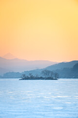This is a landscape photo of the orange sky at dawn, a frozen lake, and a small island in the distance. Generative AI
