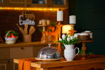 Easter cupcakes on wooden stand on kitchen table with decorative eggs, tulips and candles