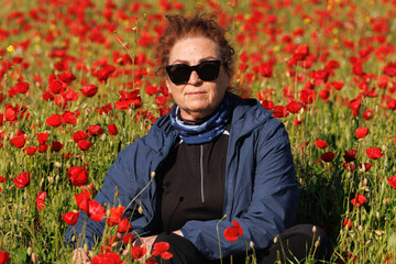 Retrato de mujer con gafas de sol sentada en campo de amapolas, España