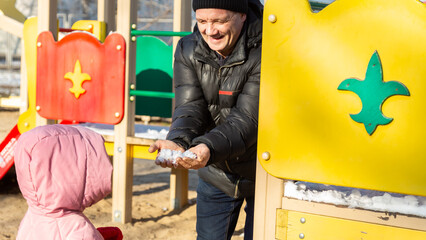 Grandfather playing with his granddaughter on the playground in the park in winter