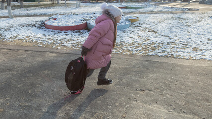 Grandfather walks with his granddaughter after school in the park in winter
