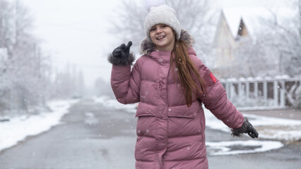Happy child walks down the street and enjoys the first snow in winter