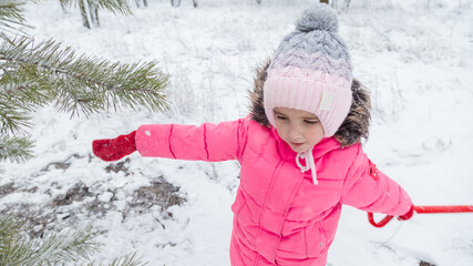 Small girl playing with snow. Child in winter forest on snowy cold day.