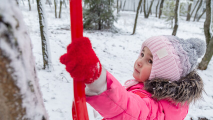 Small girl playing with snow. Child in winter forest on snowy cold day.