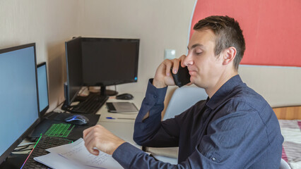 Man working online from home, using computer and having phone conversation with business partner