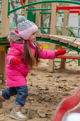 Obraz premium Little girl having fun on playground. Happy healthy little child climbing, swinging and sliding on different equipment. Child on cold day in colorful clothes outdoors