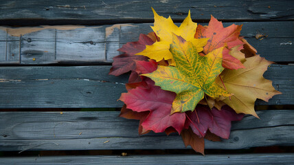 Obraz premium A stack of crisp, colorful autumn leaves arranged on a weathered wooden table.