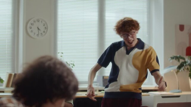 Young curly haired man smiling and dancing happily with excitement, celebrating business achievement together with supportive team applauding him in modern office