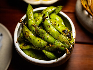 Bowl of seasoned edamame. The edamame are grilled and smoky texture. With black pepper, chili flakes.