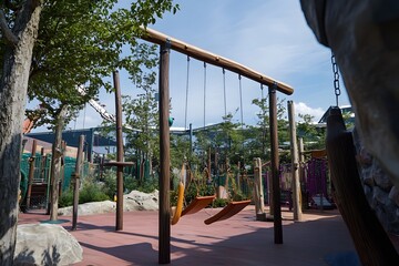 Playground with wood beams, suspended swings, greenery, and blue sky