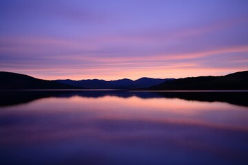 Obraz premium Purple sunset reflects on still lake with silhouetted hills background