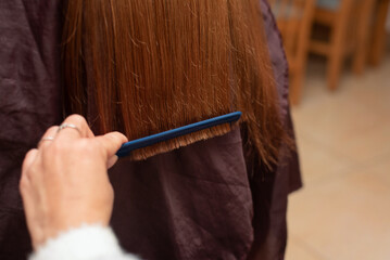 Close-up view showcasing hands combing neatly trimmed brown hair with blue comb in a salon setting, highlighting grooming and hygiene practices. Mom cuts her daughter's hair