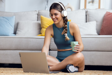 Sporty woman using laptop while listening to music with headphone sitting on the floor at home