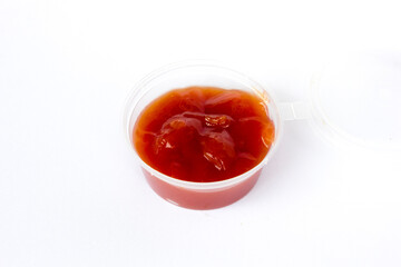 A transparent plastic cup filled with tomato ketchup on white background