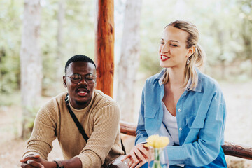 Two friends share a relaxed conversation in a wooded area, enjoying the outdoors and companionship. The ambience is serene and cheerful, highlighting friendship and nature.