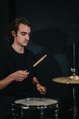 A drummer with a focused expression playing on a drum set during a live band rehearsal in a dark studio setting, emphasizing musical practice, creativity, and artistry in music performance.
