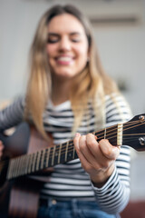 Fototapeta premium Pretty influencer woman playing guitar and strumming in the living room at home