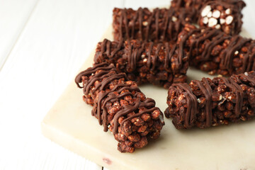 Delicious chocolate puffed rice bars on white wooden table, closeup. Space for text