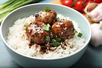 Delicious rice with meatballs, sauce and green onions on blue wooden table, closeup