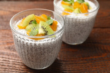 Delicious chia pudding with kiwi, peach and mint in glasses on wooden table, closeup