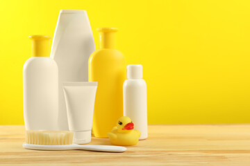 Baby cosmetic products and bath accessories on wooden table against yellow background. Space for text