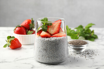 Delicious chia pudding with strawberries and mint in glass on white marble table, closeup