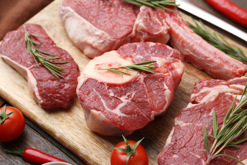 Pieces of raw beef, rosemary and tomatoes on wooden table, closeup