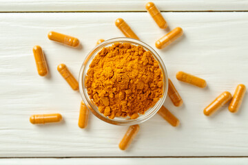 Turmeric capsules and powder on white wooden table, flat lay