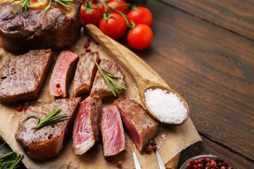 Pieces of delicious beef meat, spices and tomatoes on wooden table, closeup. Space for text