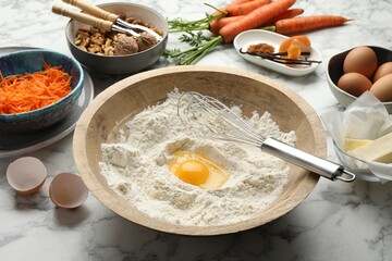 Making carrot cake. Bowl with flour, egg, whisk and other ingredients on white marble table, closeup