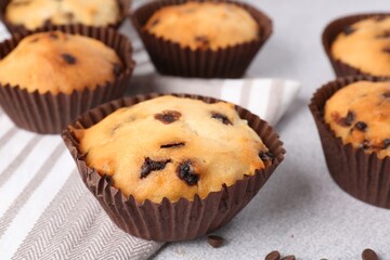 Delicious muffin with chocolate chips on light grey table, closeup