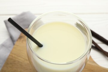 Delicious vanilla milk in glass and pods on white table, closeup