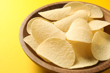 Tasty potato chips in bowl on yellow background, closeup