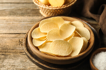 Tasty chips, salt and raw potatoes on wooden table, closeup