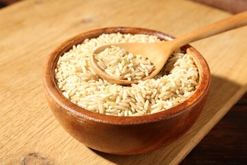 Brown rice and spoon in bowl on wooden table, closeup