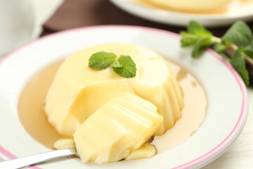 Delicious pudding with caramel sauce and mint served on white table, closeup