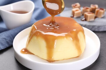 Pouring caramel sauce onto pudding on gray table, closeup